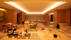 Un amplio comedor con múltiples mesas y sillas, un bufé con diversos platos y bebidas, y un diseño de techo moderno con iluminación empotrada.