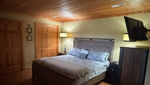 A bedroom with a bed, wooden ceiling, a TV mounted on the wall, and a wardrobe.