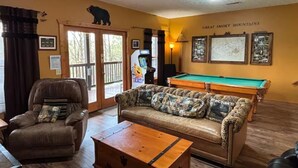 A room with a pool table, a leather sofa, a recliner, and a wooden coffee table.