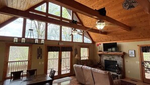 A cabin interior with a dining area, a fireplace, and large windows.