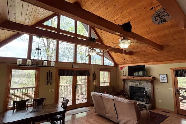 L’intérieur d’une cabane comprend un coin repas, une cheminée et de grandes fenêtres.