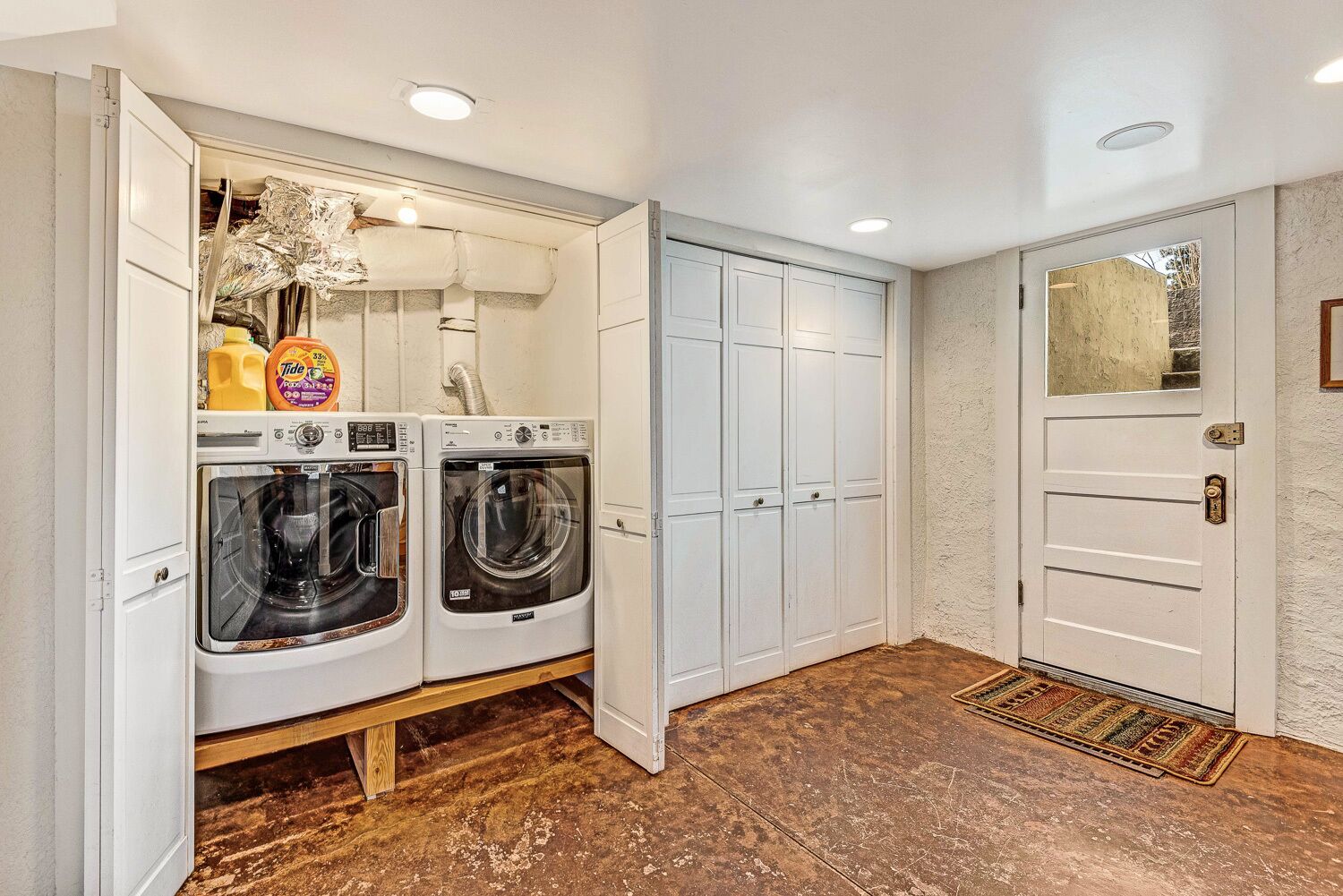 A laundry room with two front-loading washing machines, a drying rack, and a storage cabinet.