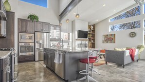 A modern kitchen with stainless steel appliances, a central island with bar stools, and a dining area with a sofa and table. - Modern Luxury I Mountain Views- central location- 4BR/3Ba (Colorado Springs)