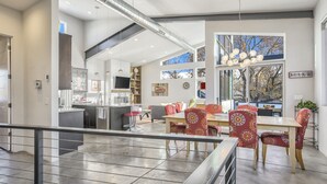 A modern kitchen with a central island, a dining area with red patterned chairs, and large windows offering views of trees. - Modern Luxury I Mountain Views- central location- 4BR/3Ba (Colorado Springs)