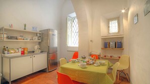 A compact kitchen with a dining area, featuring a table set for four, a refrigerator, and shelves with kitchen items. - Stilmoderno 2 rooms apartment in Siena (Siena)