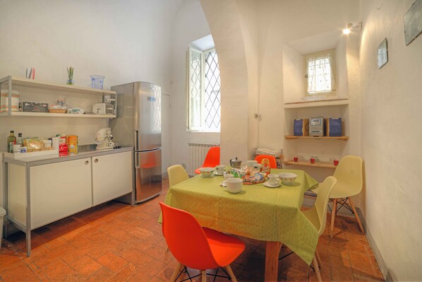 A compact kitchen with a dining area, featuring a table set for four, a refrigerator, and shelves with kitchen items.