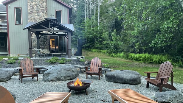 Ein gemütlicher Außenbereich mit Adirondack-Stühlen, einer Feuerstelle und einer Holzterrasse.