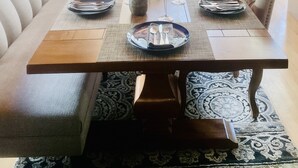 Ein Essbereich mit einem langen Holztisch, gedeckt für sechs Personen, umgeben von gepolsterten Sitzgelegenheiten.