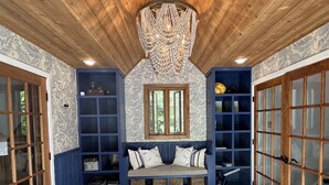 Ein Zimmer mit Holzbalkendecke, einer Kristallleuchter, einer Bank mit Kissen und einem gemusterten Teppich.