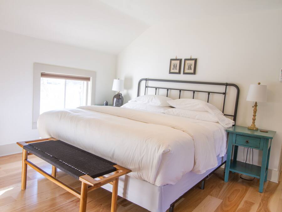 A bedroom with a bed, bedside tables, a bench, and a window.