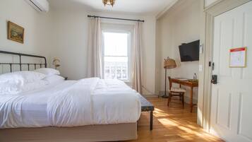 A bedroom with a large bed, a desk, a chair, a television, and a door with a sign.