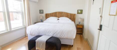 Un dormitorio con una cama grande, mesitas de noche, un banco y una ventana con cortinas.