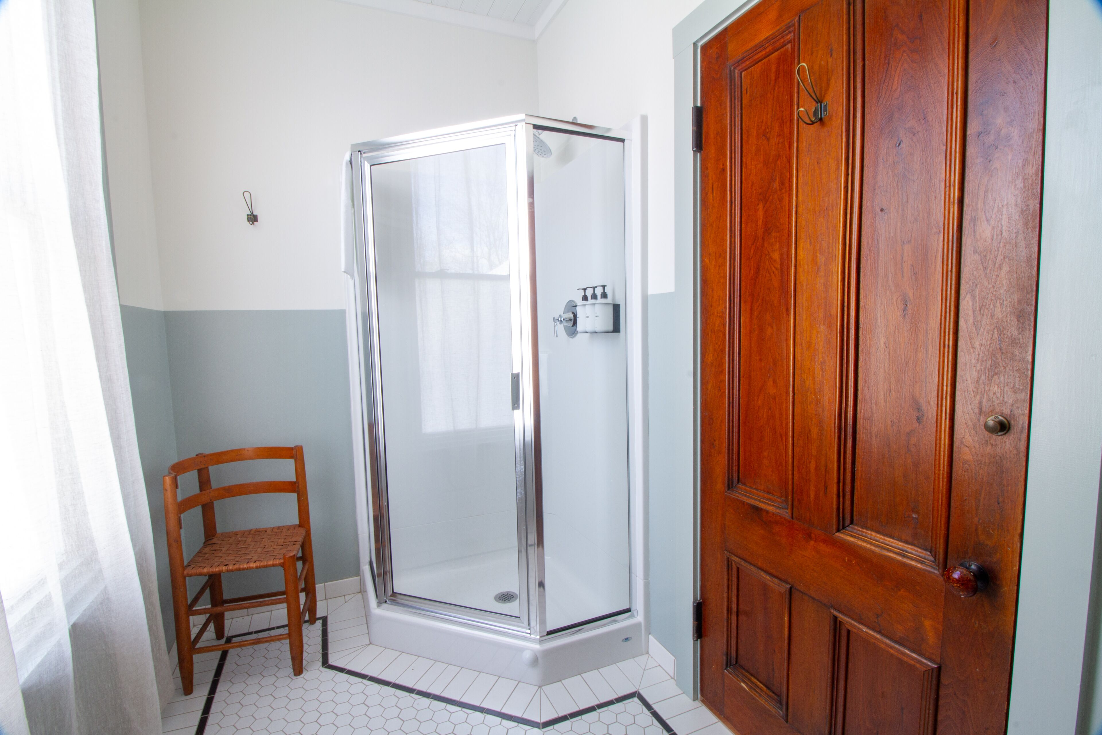 A bathroom with a shower, a wooden chair, and a wooden door.