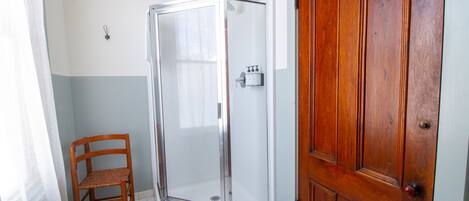 A bathroom with a shower, a wooden chair, and a wooden door.