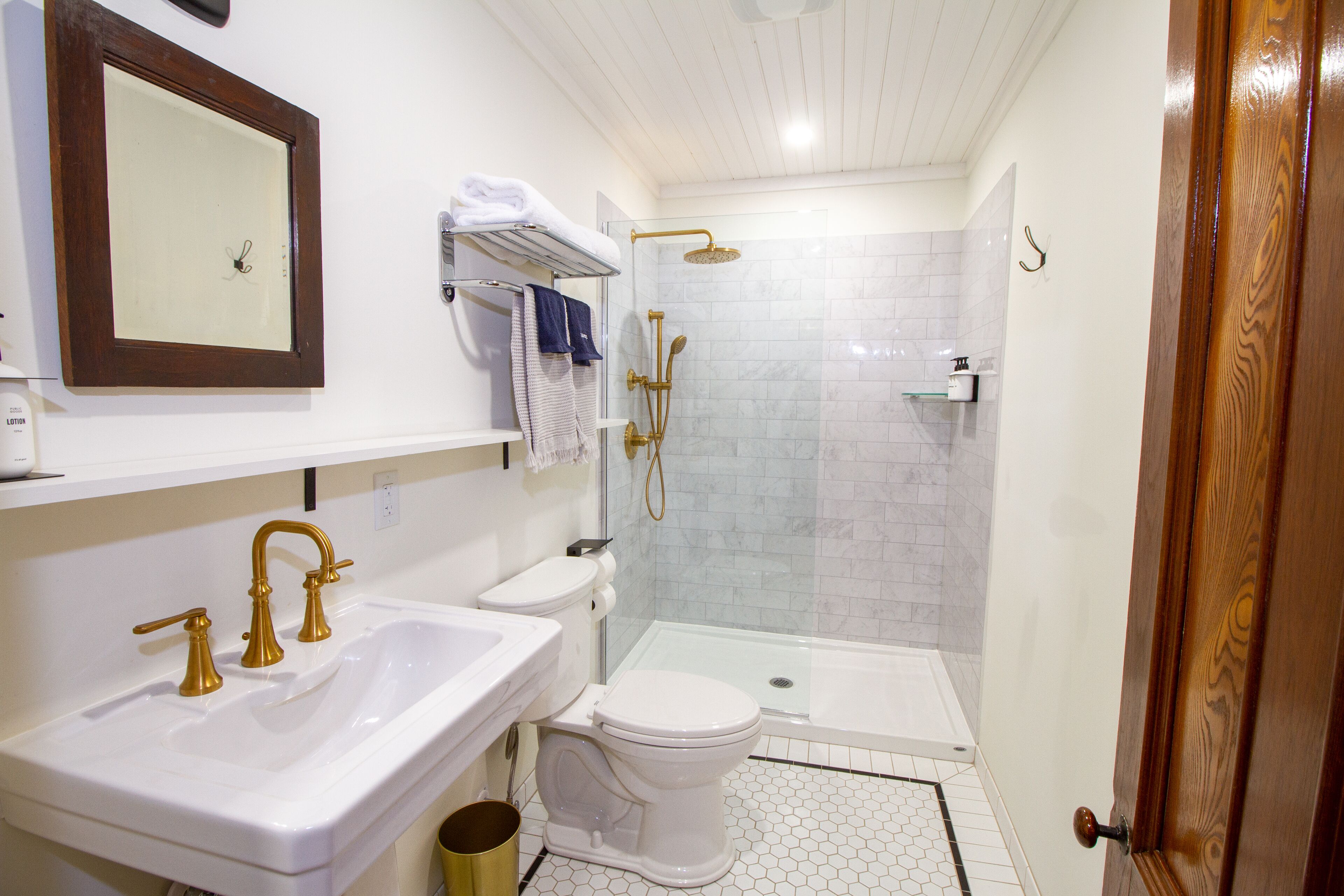 Un baño con lavamanos blanco, inodoro, ducha con puerta de vidrio y puerta de madera.