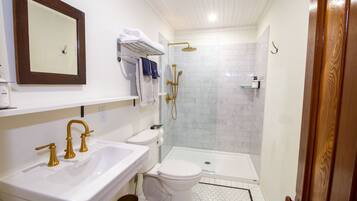 A bathroom with a white sink, a toilet, a shower with a glass door, and a wooden door.
