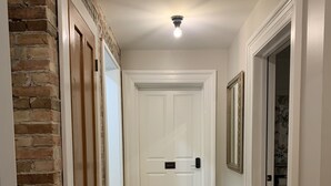 A hallway with a herringbone wooden floor, white doors, and a brick wall on one side. - Pert House (Potsdam)