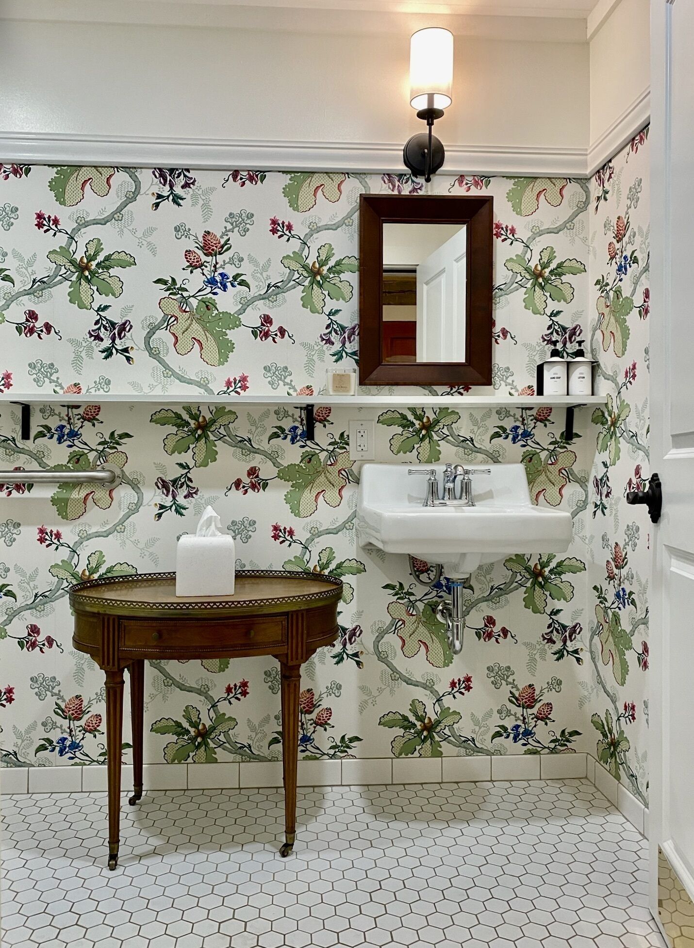 Une salle de bain avec un papier peint à motifs floraux, un meuble-lavabo en bois, un évier et un miroir.