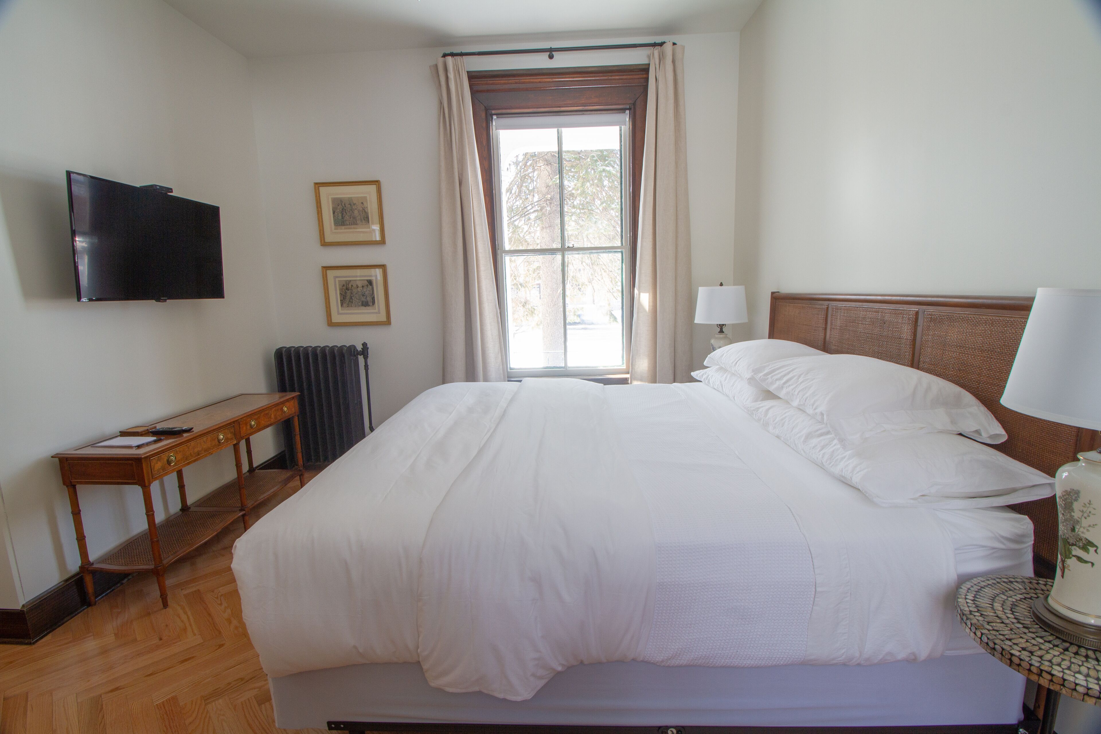 A hotel room with a large bed, a television mounted on the wall, a small table, and a window with curtains.