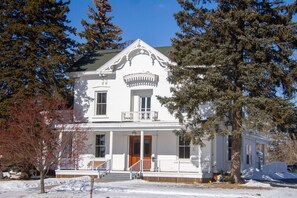 A white two-story house with a front porch, a central entrance, and a small balcony.