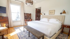 A bedroom with a large bed, a bench, a desk, a chair, a dresser, a TV, and a bookshelf. - Pert House (Potsdam)