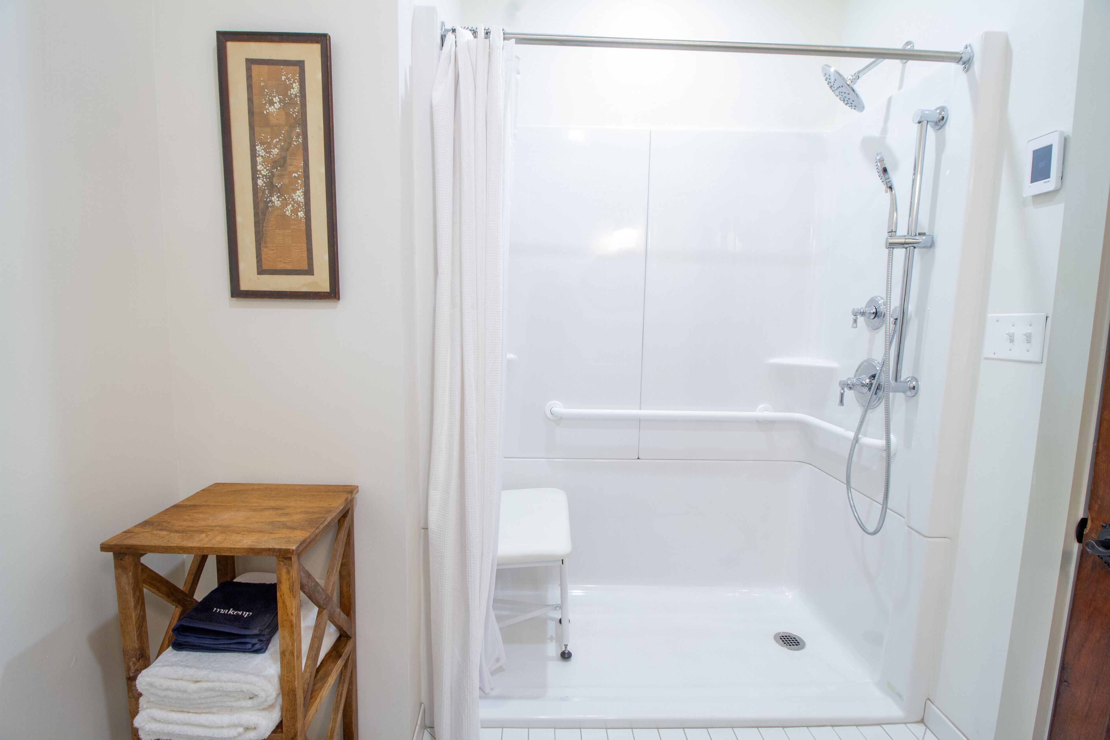 A walk-in shower with a white tiled wall, a wooden bench, and a framed picture on the wall.