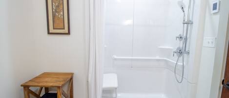 A walk-in shower with a white tiled wall, a wooden bench, and a framed picture on the wall.
