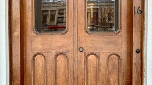 A wooden double door with a number '16' on the right side, a small window on the left, and a metal handle. - Pert House (Potsdam)