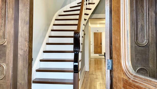 A wooden staircase with white steps and a dark handrail leading to a landing. - Pert House (Potsdam)