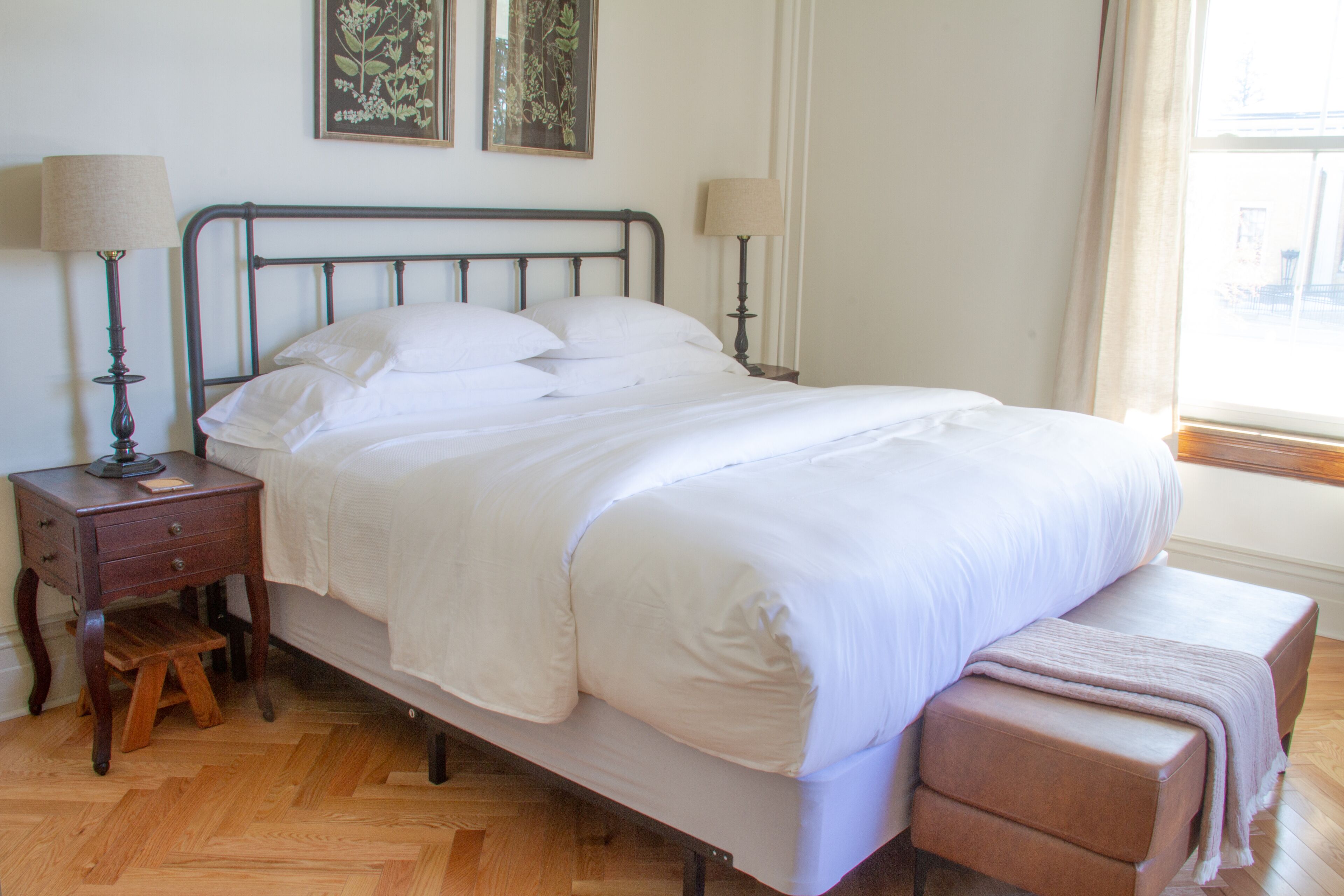 A neatly made bed with white linens, a wooden nightstand with a lamp, and a bench at the foot of the bed.
