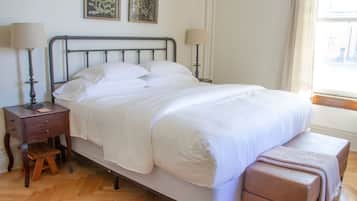 A neatly made bed with white linens, a wooden nightstand with a lamp, and a bench at the foot of the bed.
