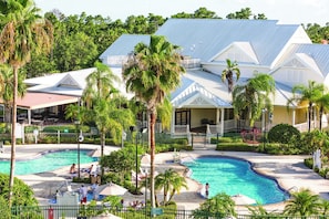 A resort with two swimming pools, surrounded by palm trees and a building with a blue roof.