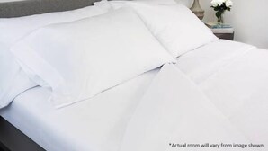 A neatly made bed with white bedding, a gray headboard, and a small bedside table with a vase of white flowers. - Club Wyndham Kingstown Reef - Studio Suite (Orlando)