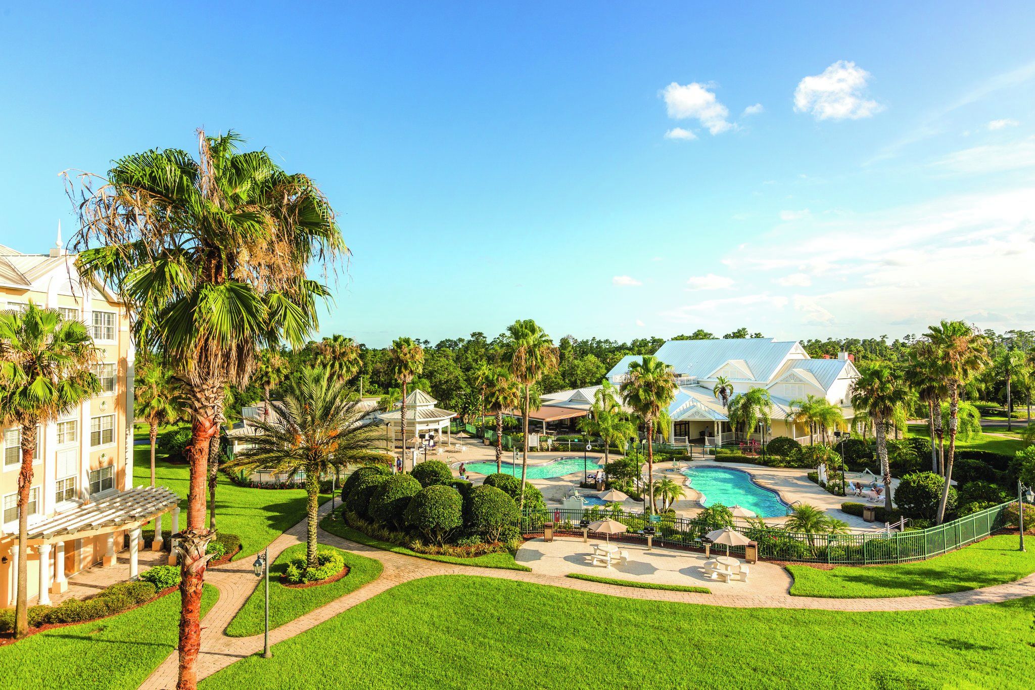 Un resort con piscina, palmeras y un edificio grande de fachada blanca.