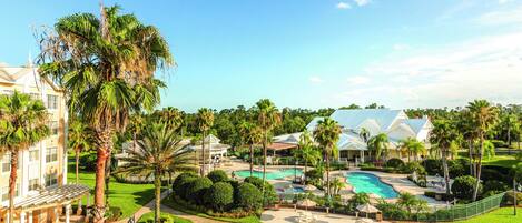 Un resort con piscina, palmeras y un edificio grande de fachada blanca.