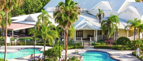 A resort with two swimming pools, surrounded by palm trees and a building with a blue roof.