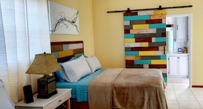 A bedroom with a bed, bedside table, lamp, and a colorful wall panel.
