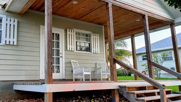 A house with a porch, two white chairs, and a wooden staircase.