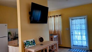 A compact kitchen with a refrigerator, a dining table with a painting, and a TV mounted on the wall.