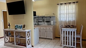 A compact kitchen with a dining area, a TV mounted on the wall, and a small table with chairs.