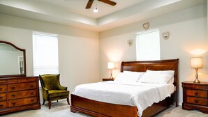 A bedroom with a wooden bed, two nightstands, a green armchair, a dresser, and a ceiling fan. - Clean & Cozy new Home, 30 mins to George Bush INTL/ downtown 5 mins to woodlands (Conroe)