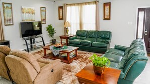 A living room with a green sofa, beige armchairs, a TV, and artwork on the walls. - Clean & Cozy new Home, 30 mins to George Bush INTL/ downtown 5 mins to woodlands (Conroe)