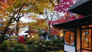 A traditional Japanese building with a wooden exterior, surrounded by a garden with various plants and a small pond. - Takei Ryokan (Nagano)