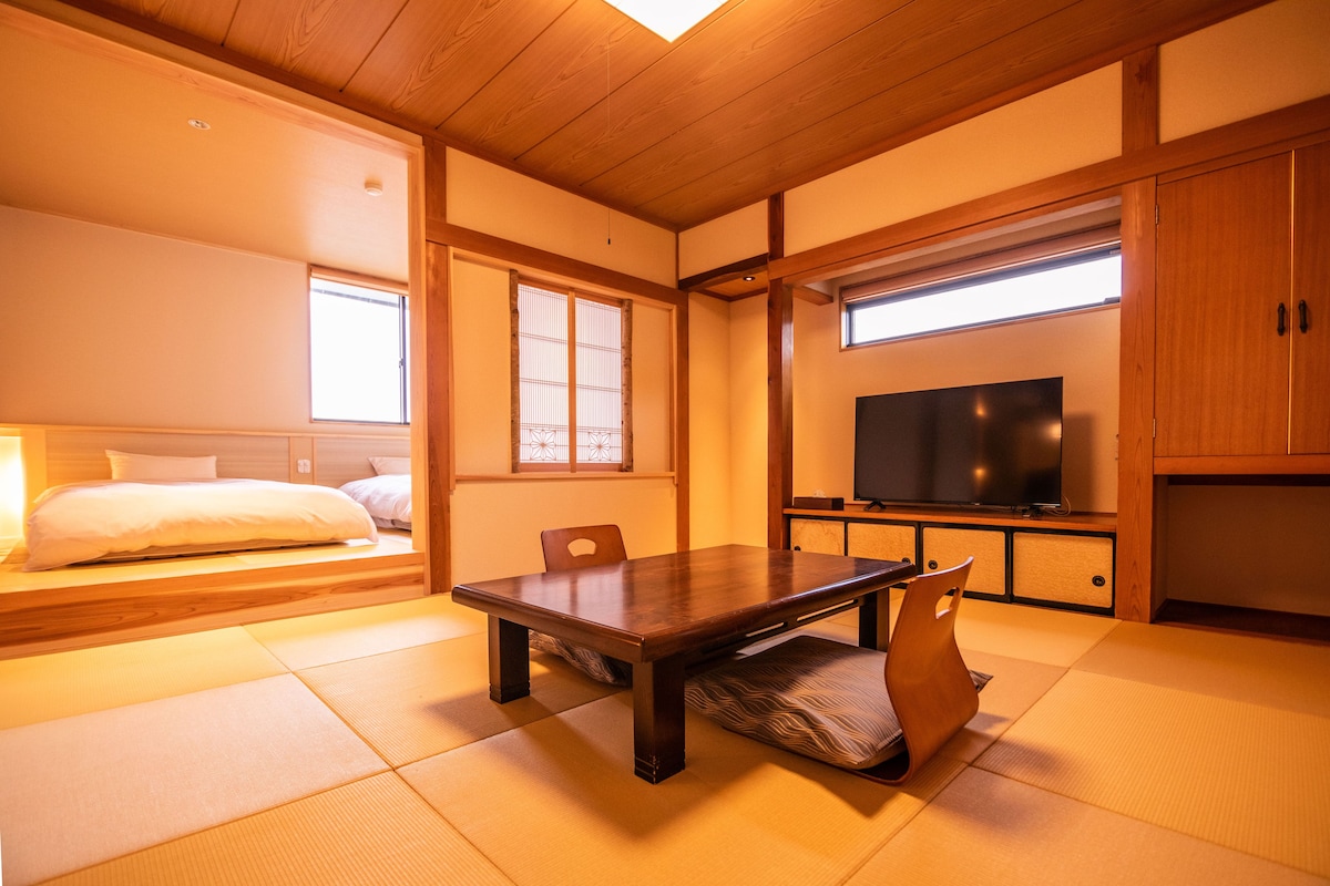 A traditional Japanese room with tatami flooring, a low wooden table, a television, and sliding doors.