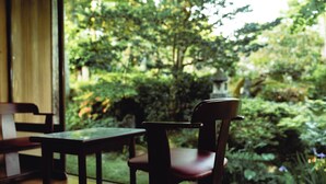 A wooden chair and table inside a room with a view of a lush garden. - Takei Ryokan (Nagano)