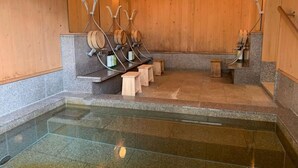 A stone-floored indoor pool with wooden benches and a wooden wall. - Takei Ryokan (Nagano)