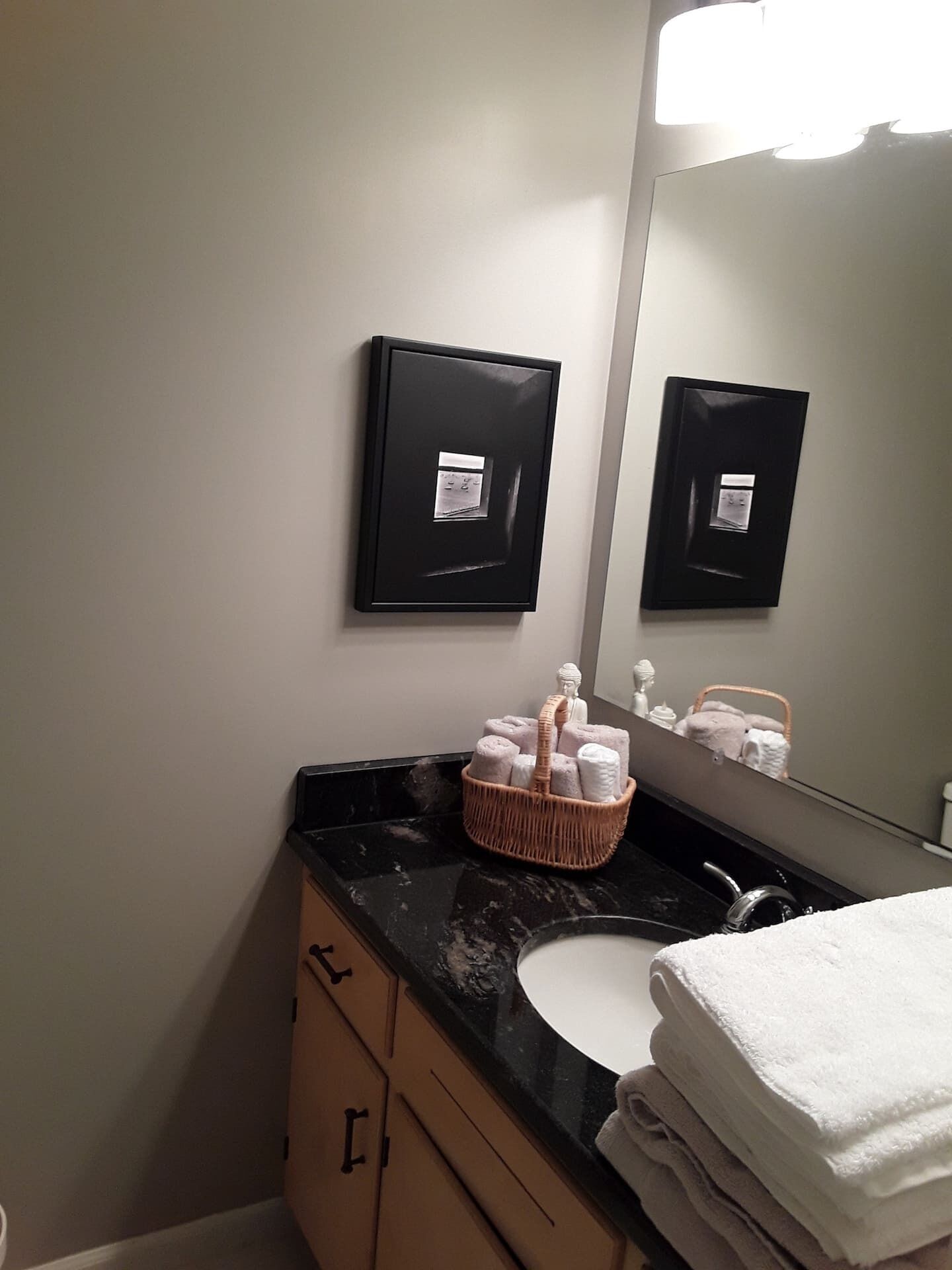 A bathroom with a black countertop, a white sink, a mirror, and a wall-mounted dispenser.