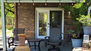 Une terrasse couverte avec deux fauteuils en osier, un grand bac à plantes et un élément décoratif aquatique.