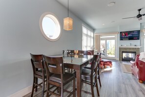 Een eethoek met een rechthoekige tafel en zes stoelen, een ronde spiegel aan de muur en een plafondventilator.