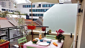 Ein Balkon mit Esstisch, umgeben von Blumentöpfen und einem großen Fenster.